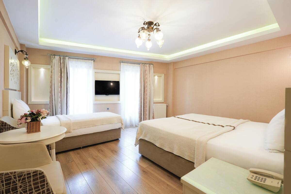 A hotel room with a bed, a sofa, a small table with a phone, and a TV on the wall.