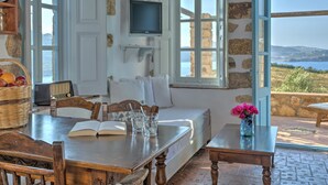 Una habitación acogedora con pared de piedra, un televisor sobre un sofá, una mesa de comedor con sillas y vistas al mar.