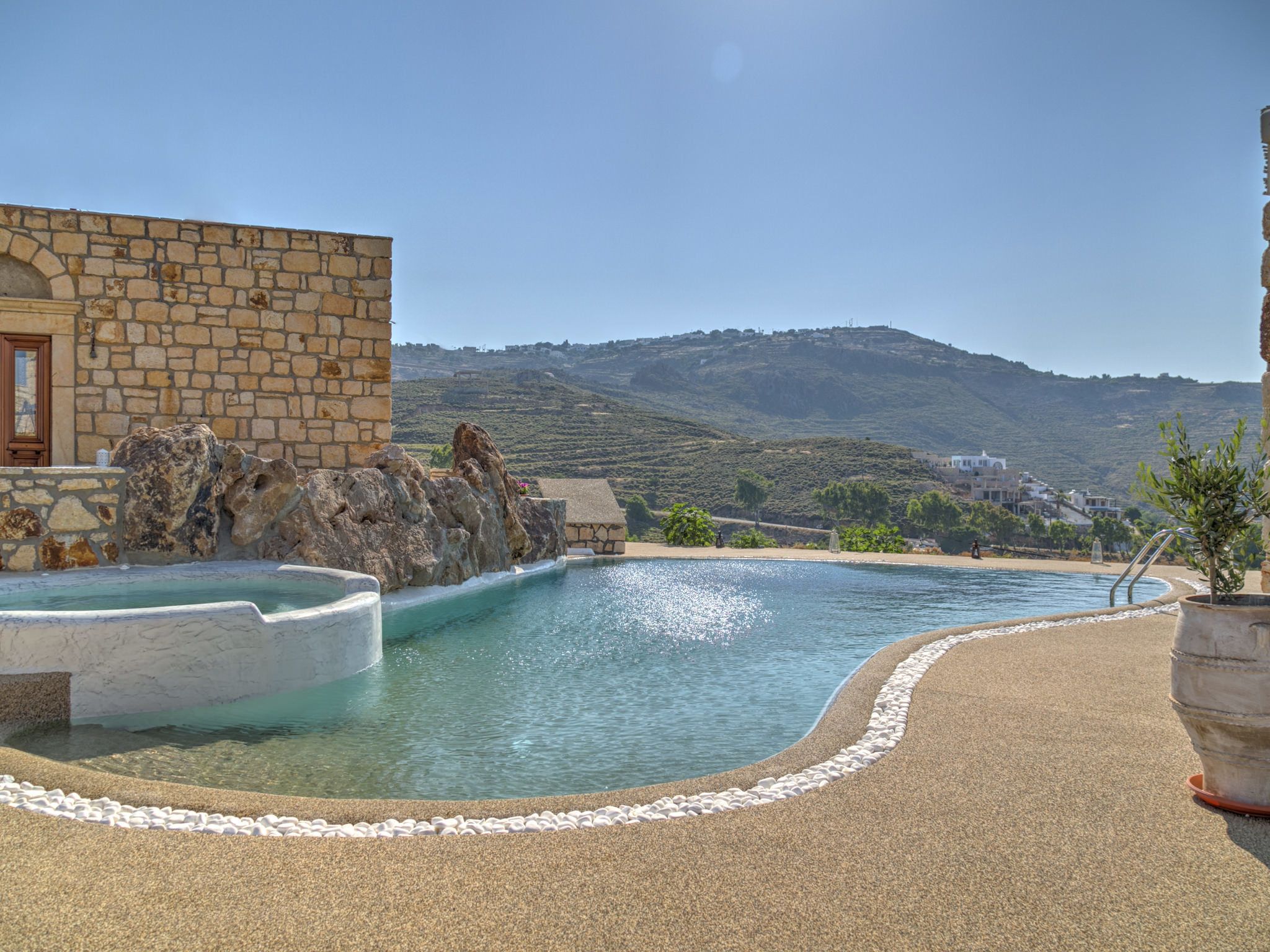 A pool with a stone wall and a view of a hill.