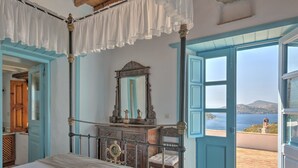 Un dormitorio con una cama grande, un aparador, un espejo y vista al mar por una puerta abierta.