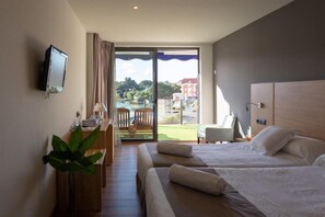 A hotel room with two beds, a desk with a computer, a TV, and a large window with a view of a pool and buildings. - Astuy (Arnuero)