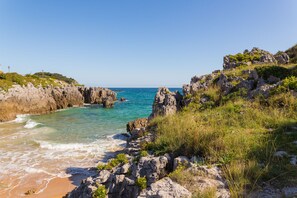 A coastal landscape with rocky cliffs, clear turquoise sea, and a sandy beach. - Astuy (Arnuero)