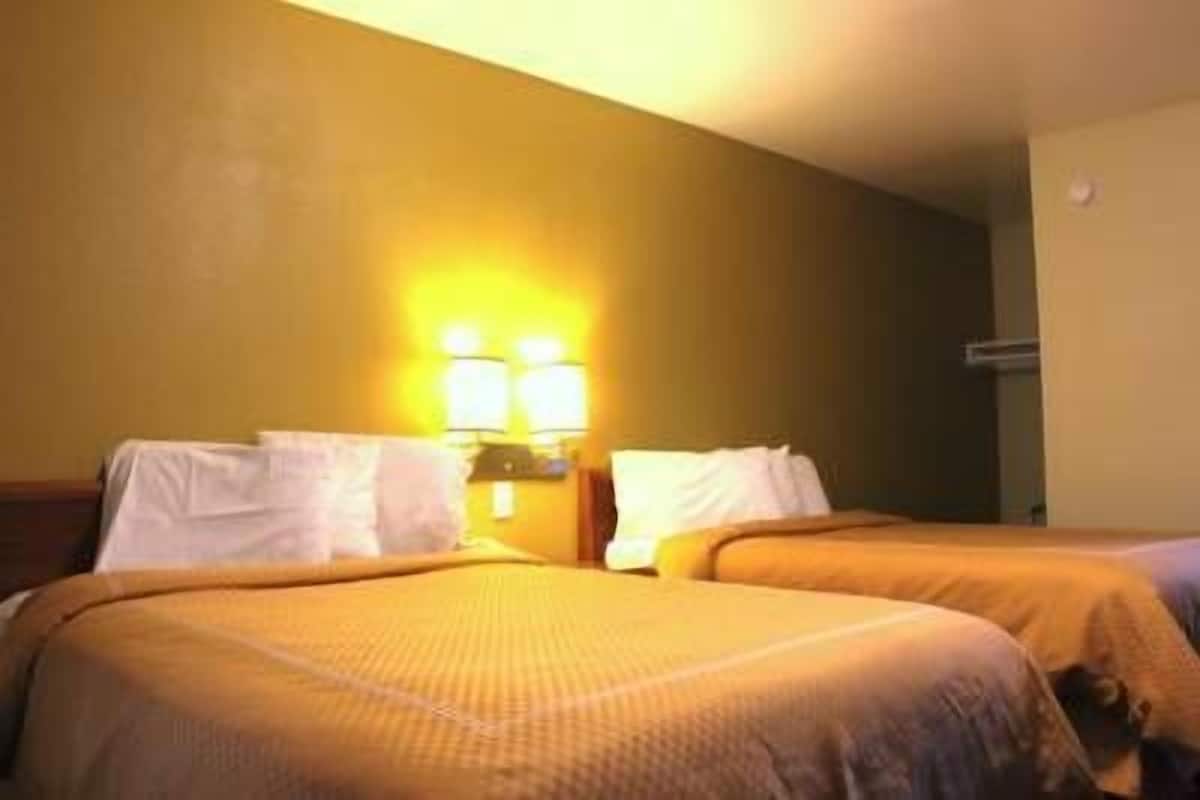 A hotel room with two beds, a nightstand, and wall-mounted lamps.