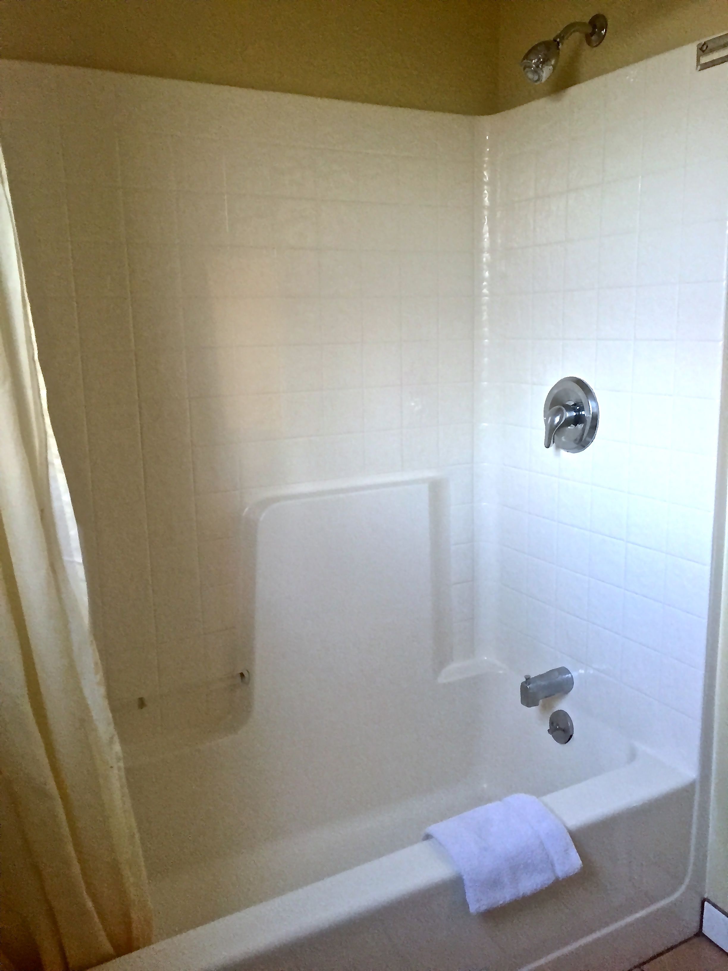 A white bathtub with a showerhead, a towel, and a curtain.