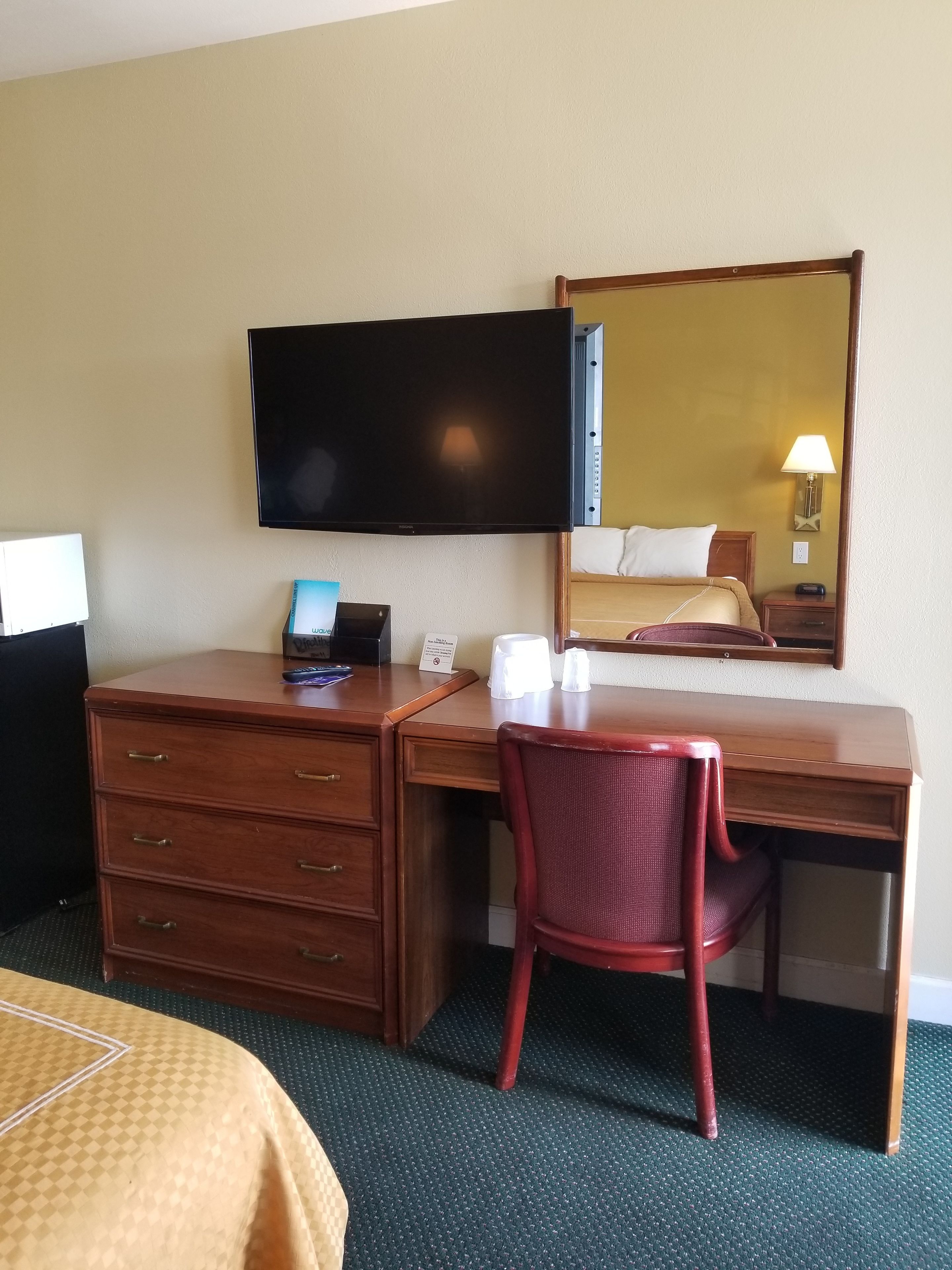 Een hotelkamer met een houten bureau, een stoel, een flatscreen televisie aan de muur en een bed met hoofdeinde.