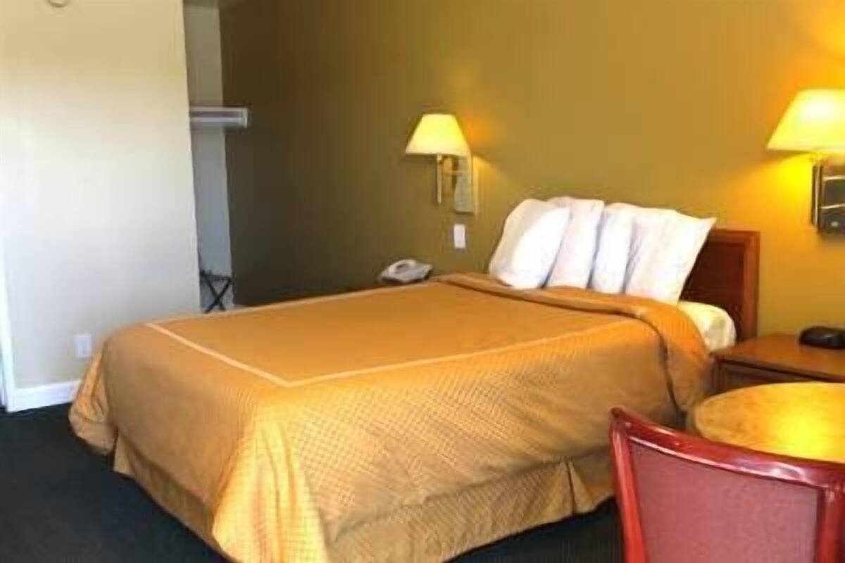 A hotel room with a large bed, two bedside lamps, a bedside phone, and a small round table with a chair.