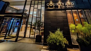 Entrada de un hotel Courtyard by Marriott con un diseño moderno, amplios ventanales de vidrio y un letrero sobre la entrada.