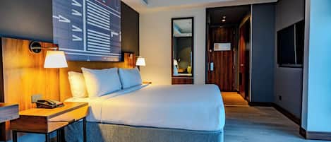A modern hotel room with a large bed, bedside lamps, a desk with a telephone, and a large abstract wall art piece.