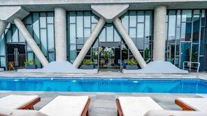 Un hotel moderno con piscina, sillas de descanso y un diseño arquitectónico único con pilares grandes.