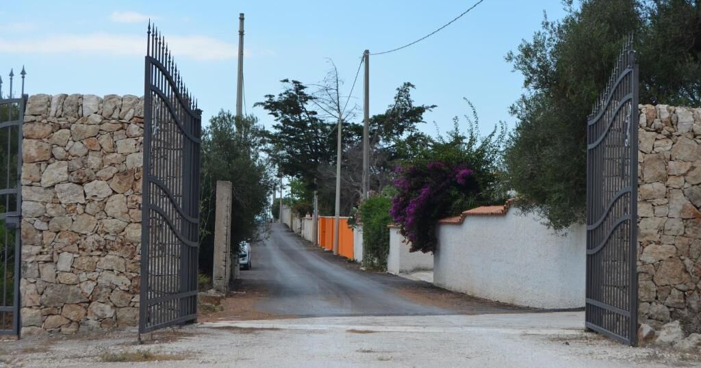 A narrow street with stone walls and metal gates.