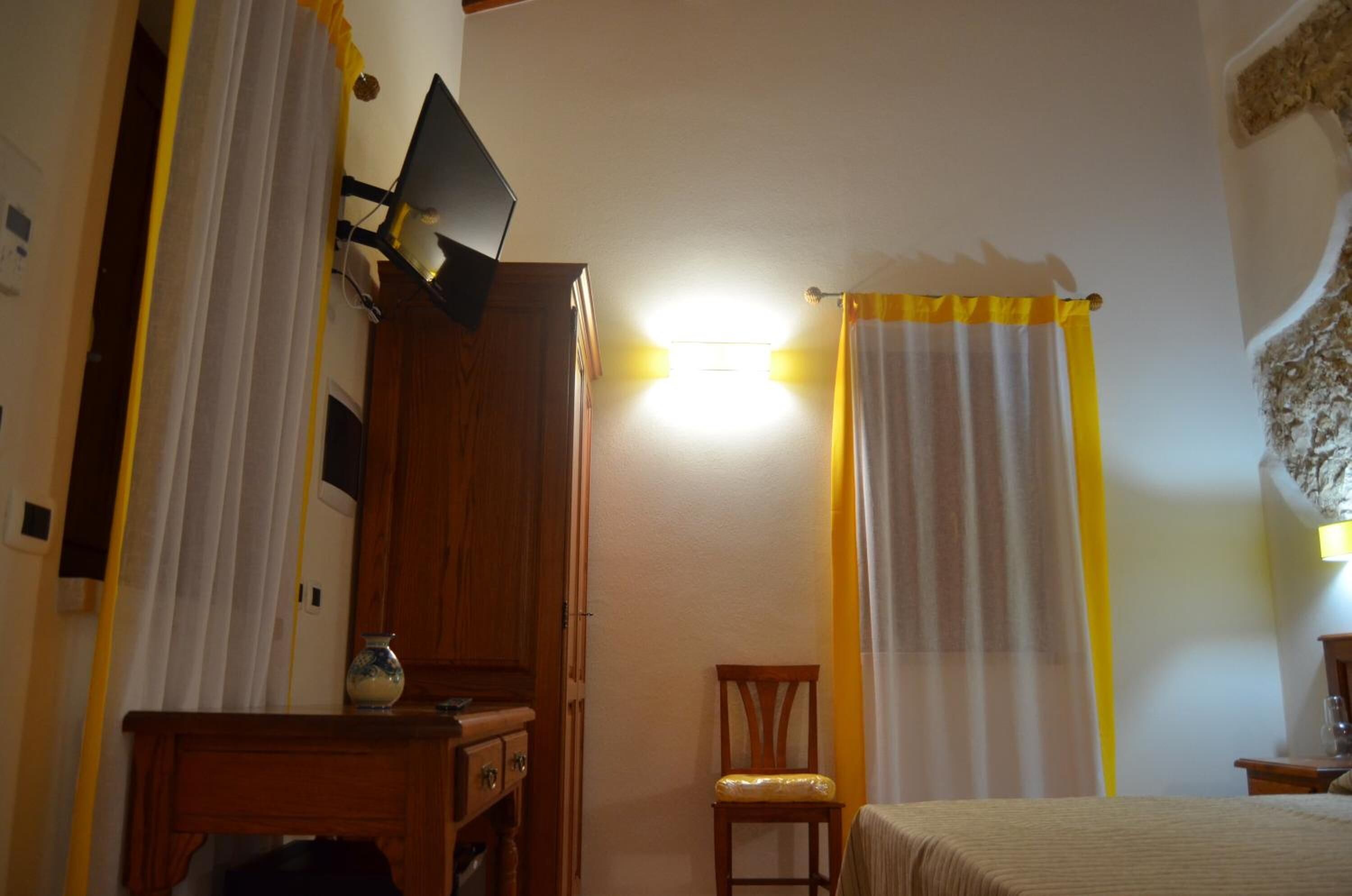 Un dormitorio con una cama, una silla de madera, un escritorio con lámpara y cortinas.