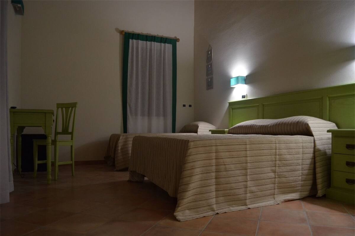Un dormitorio con dos camas, una mesita de noche verde, una silla y una lámpara de pared.