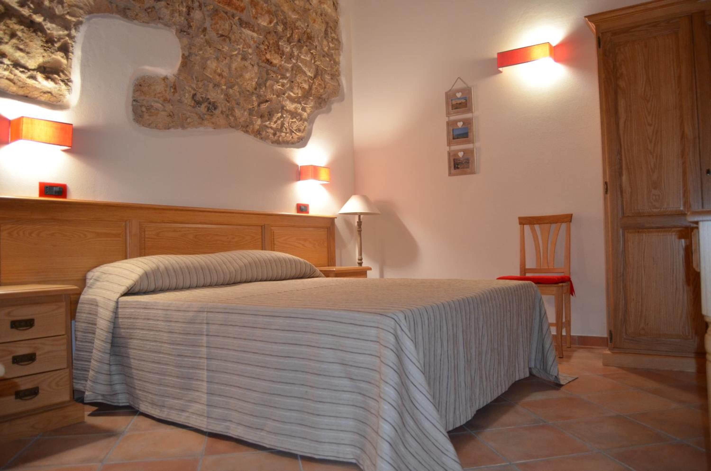 A bedroom with a bed, nightstands, a lamp, a chair, and a wooden wardrobe.