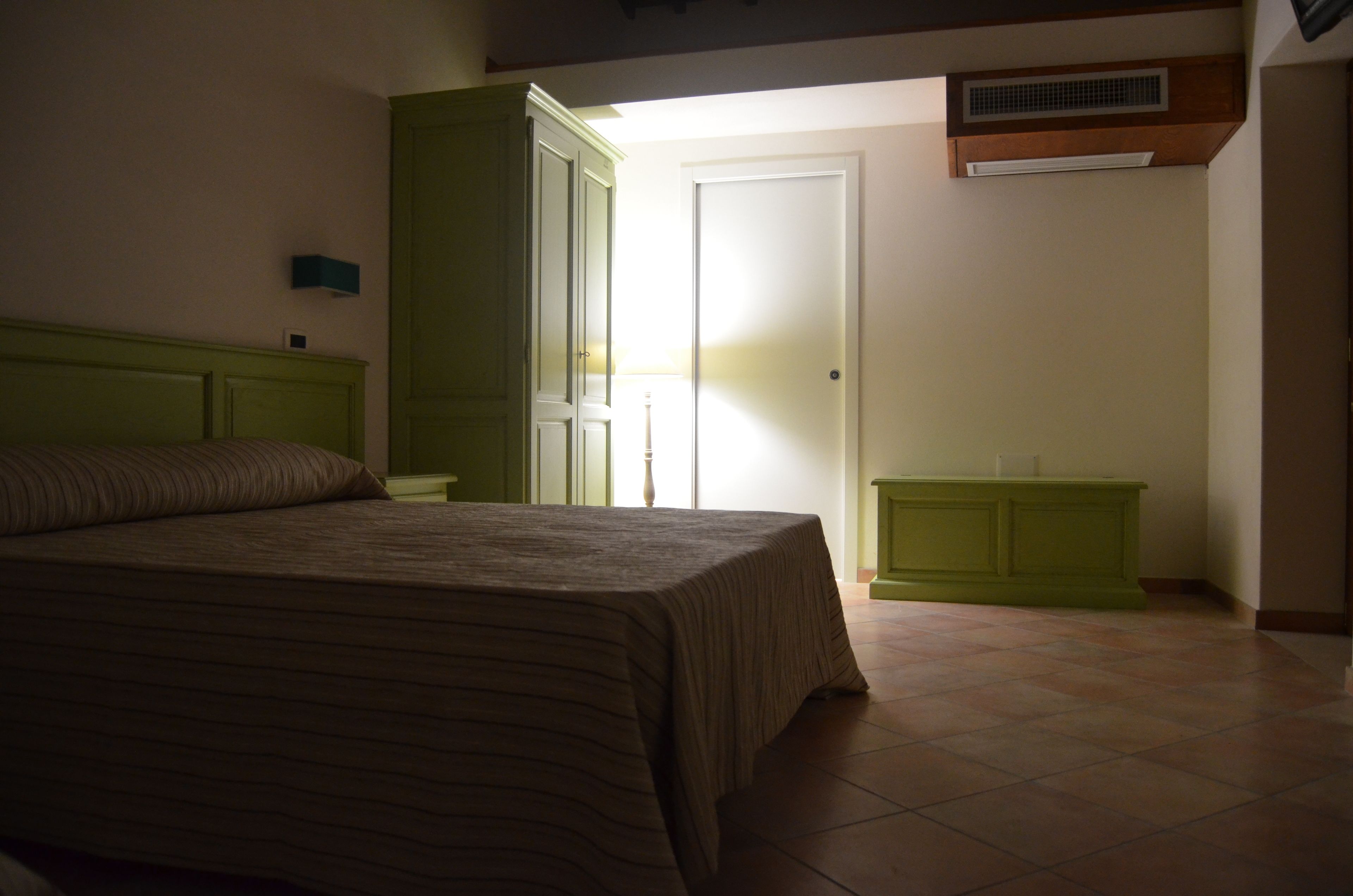 Un dormitorio con una cama, una mesita de noche, un armario verde y una puerta que da a otra habitación.