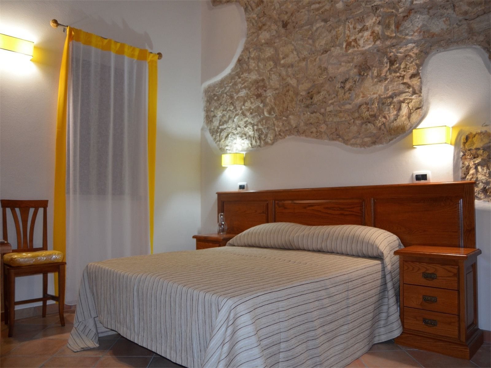 Ein Schlafzimmer mit einem Bett, Nachttischen aus Holz, einem Sessel und einer Steinwand.