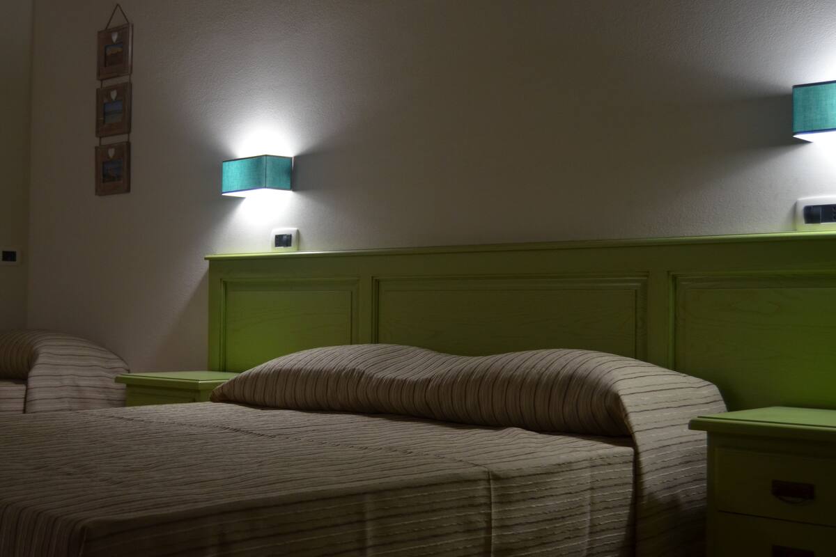 Una habitación con dos camas, cada una con una mesita de noche verde y una lámpara de pared.