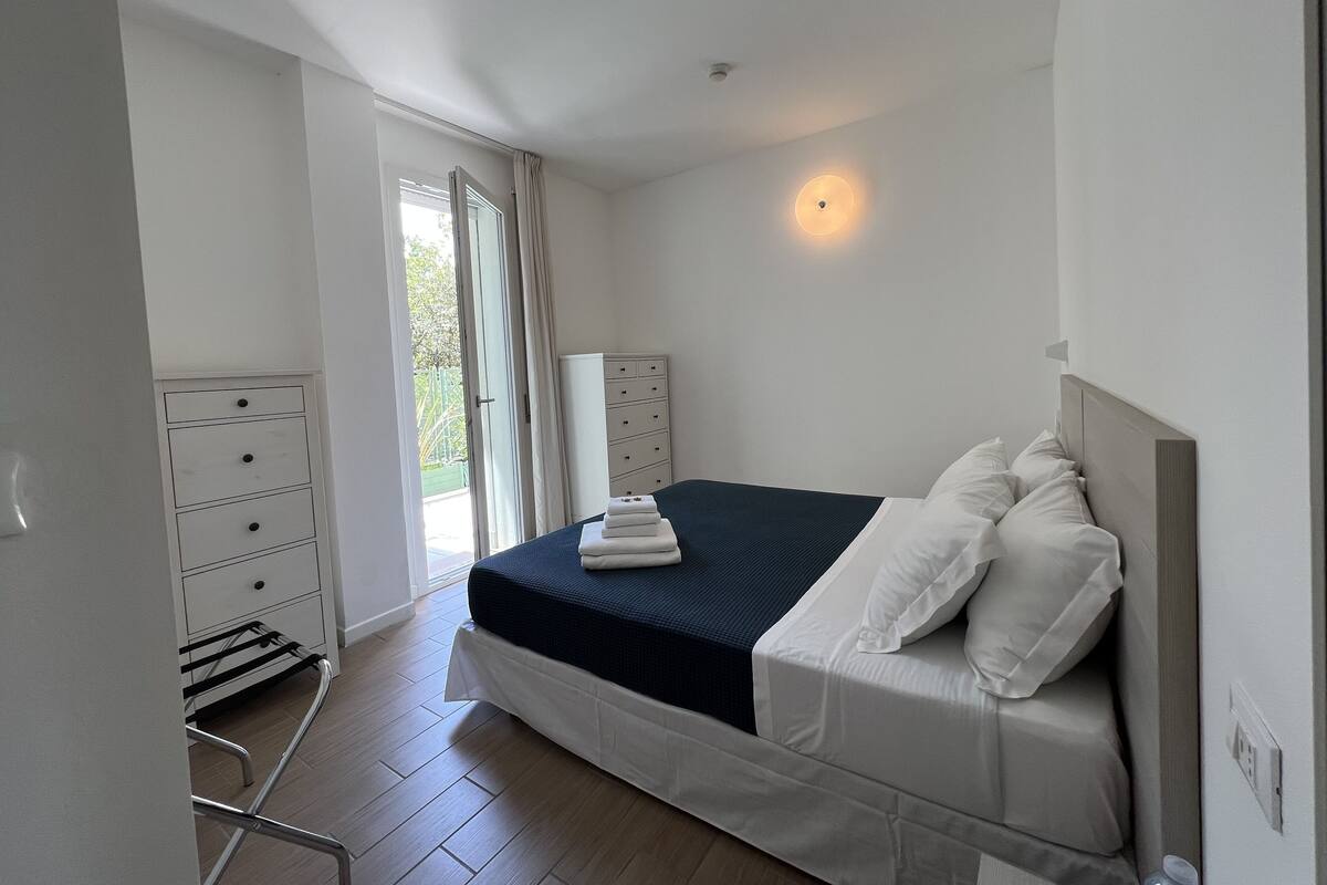A bedroom with a bed, a dresser, a radiator, and a window with curtains.