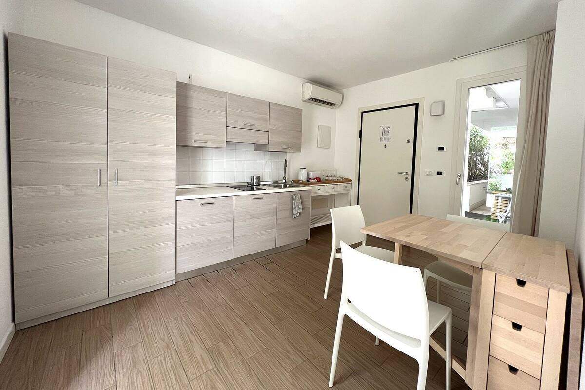 A modern kitchen with light wood cabinets, a central island, and a dining area with a wooden table and white chairs.