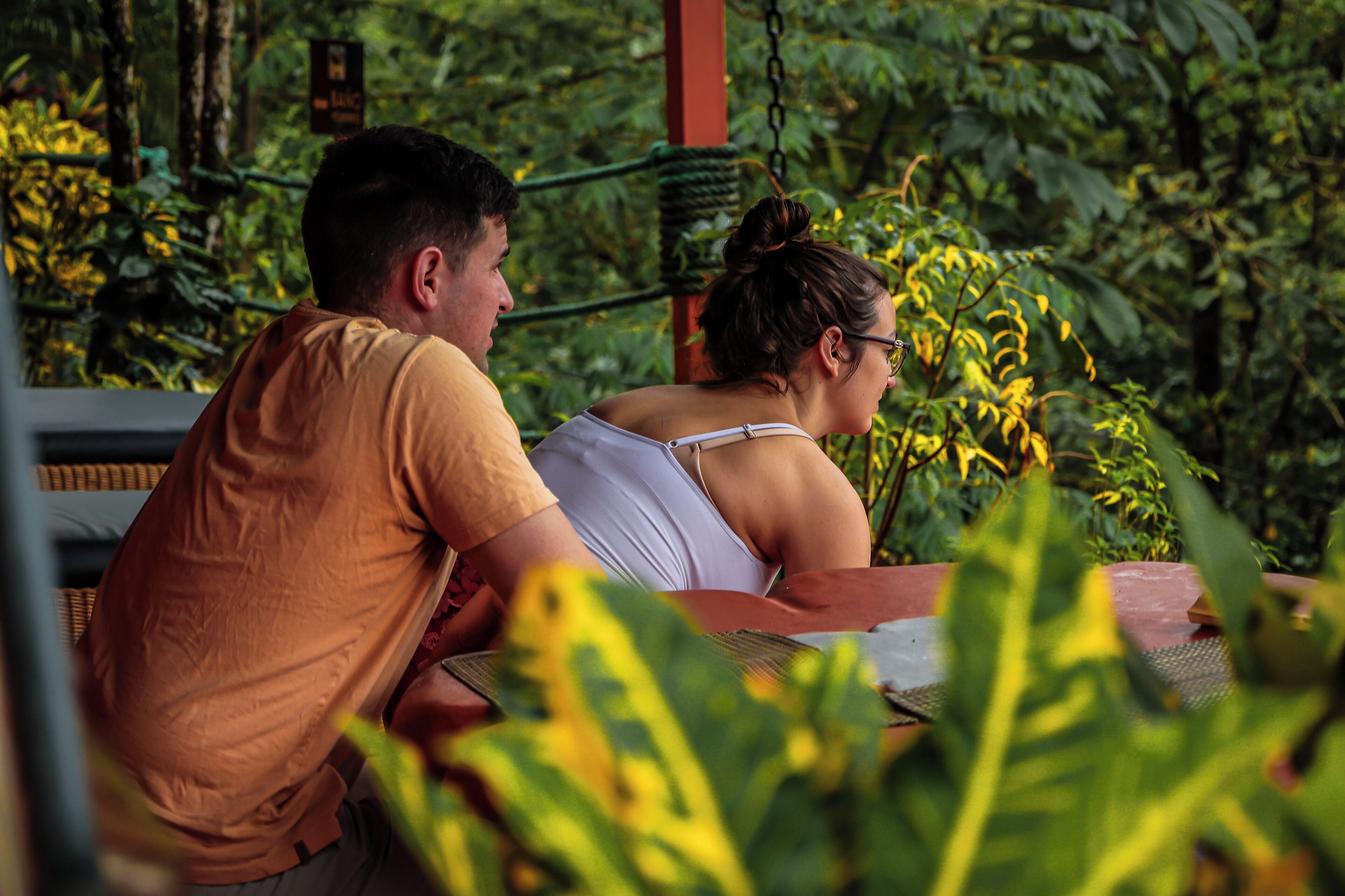 A couple seated at an outdoor table with lush greenery in the background.