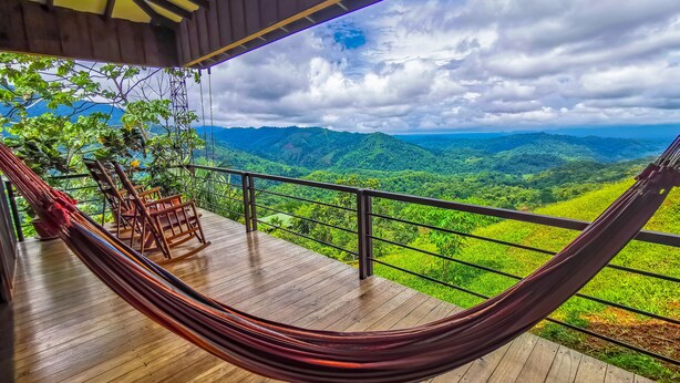 A hammock on a wooden deck with a view of lush green hills and a cloudy sky. - Santa Juana Lodge and Nature Reserve (Naranjito)