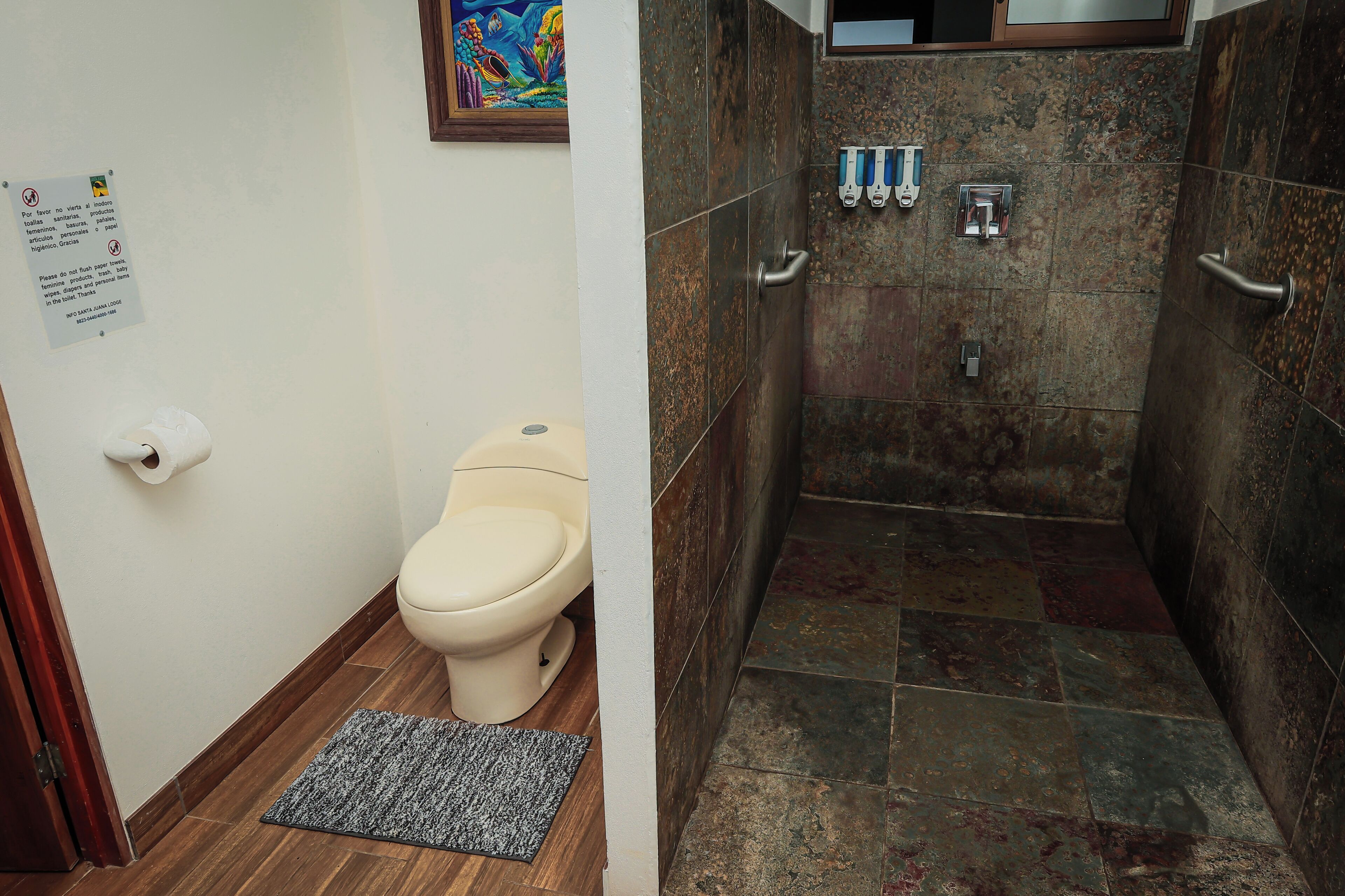 Un baño con inodoro, ducha con puerta de cristal y dispensador de gel antibacterial.