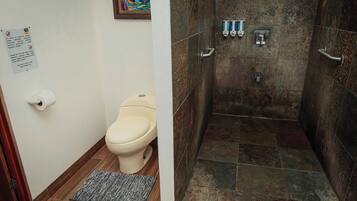 Un baño con inodoro, ducha con puerta de cristal y dispensador de gel antibacterial.
