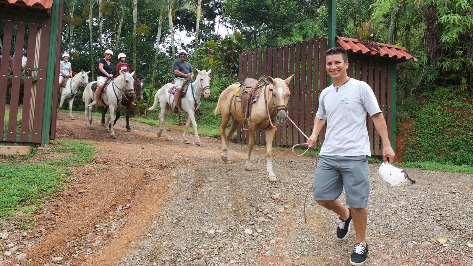 A man walking with a horse and people riding horses on a dirt path.