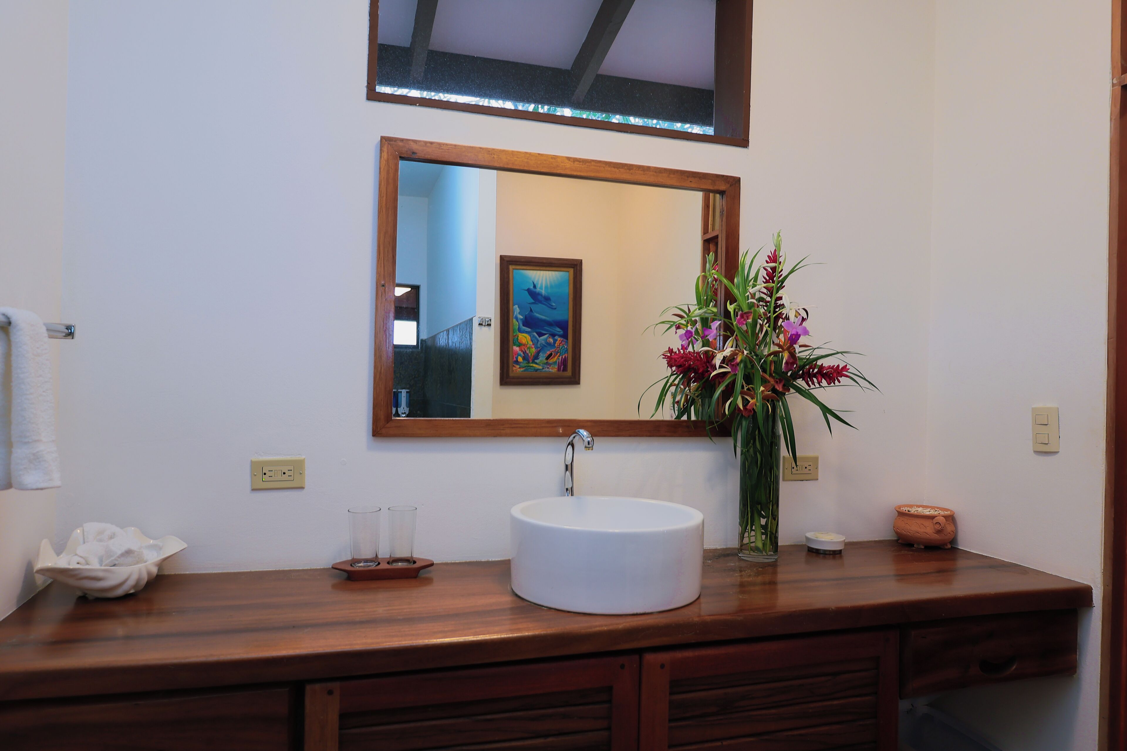 Een badkamer met een houten wastafel, een witte wasbak, een spiegel en een bloemenvaas.