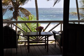 Une terrasse en bois avec une table et des chaises, donnant sur une plage bordée de palmiers et sur l’océan.
