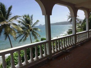 Un balcon abrité offrant une vue sur la mer et les palmiers.