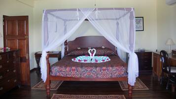 A four-poster canopy bed with a floral bedspread, a nightstand with a lamp, and a wooden dresser.
