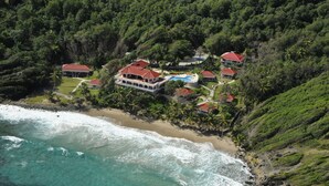An aerial view of a coastal resort with multiple buildings, a beach, and lush greenery. - Petite Anse Hotel (St. Patrick)