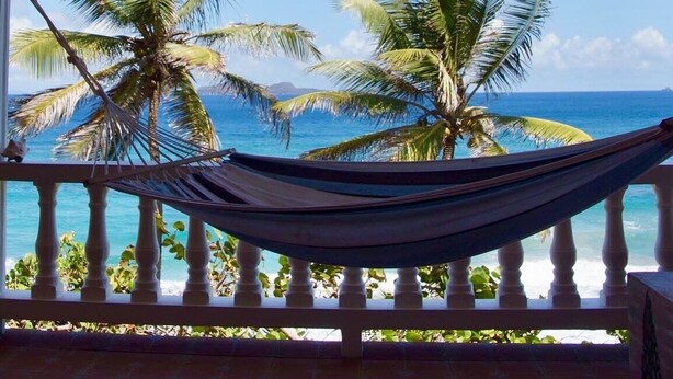 Un hamac sur un balcon avec vue sur l’océan et les palmiers.