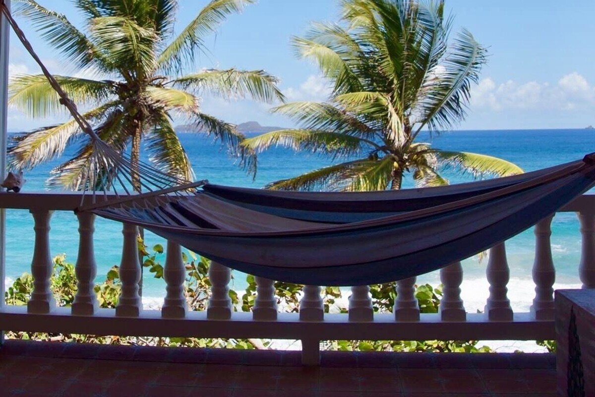 A hammock on a balcony with a view of the ocean and palm trees.