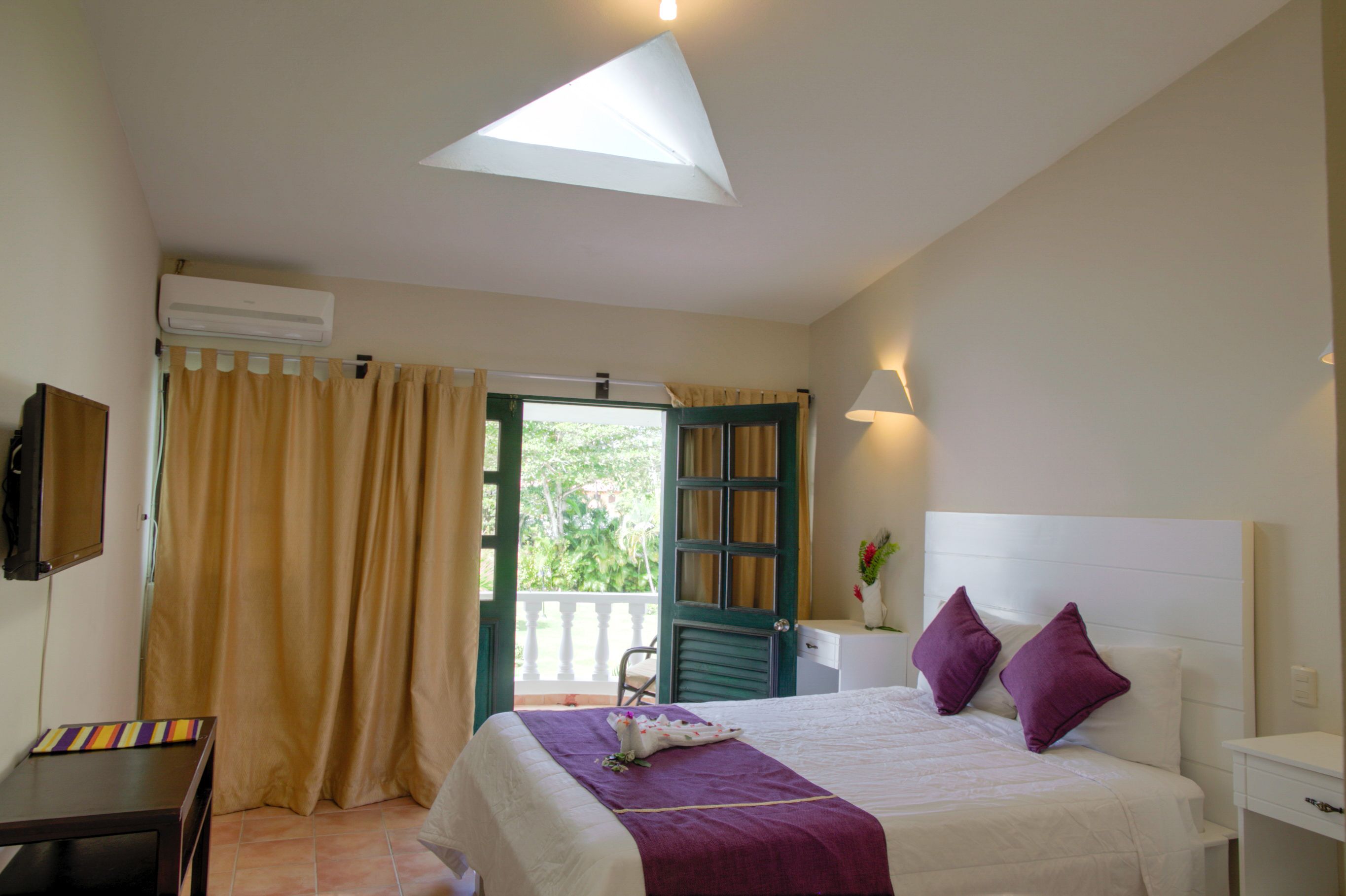 A bedroom with a bed, a desk, a TV, and a window with curtains.