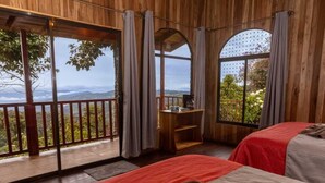 A wooden cabin room with two beds, a desk, and large windows offering a view of the outdoors. - Paraíso Quetzal Lodge (Copey)