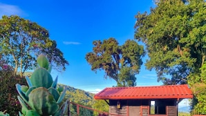 A small wooden cabin with a red roof, surrounded by lush greenery and trees. - Paraíso Quetzal Lodge (Copey)