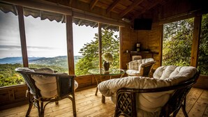 A wooden deck with wicker chairs and a glass table, overlooking a mountainous landscape. - Paraíso Quetzal Lodge (Copey)