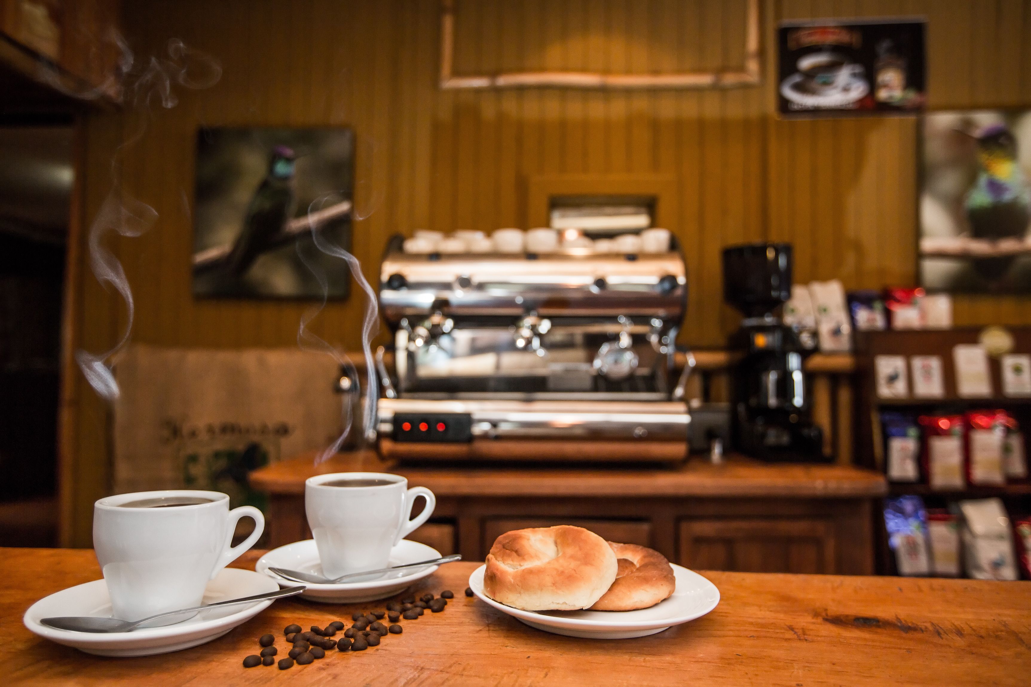 A coffee shop interior with espresso machines, coffee cups, and pastries on a wooden table.