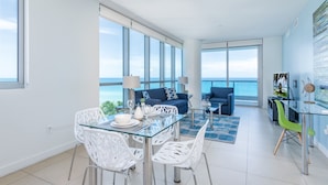 Una sala moderna con una mesa de comedor de cristal, sillas blancas, un sofá azul y vista al océano.