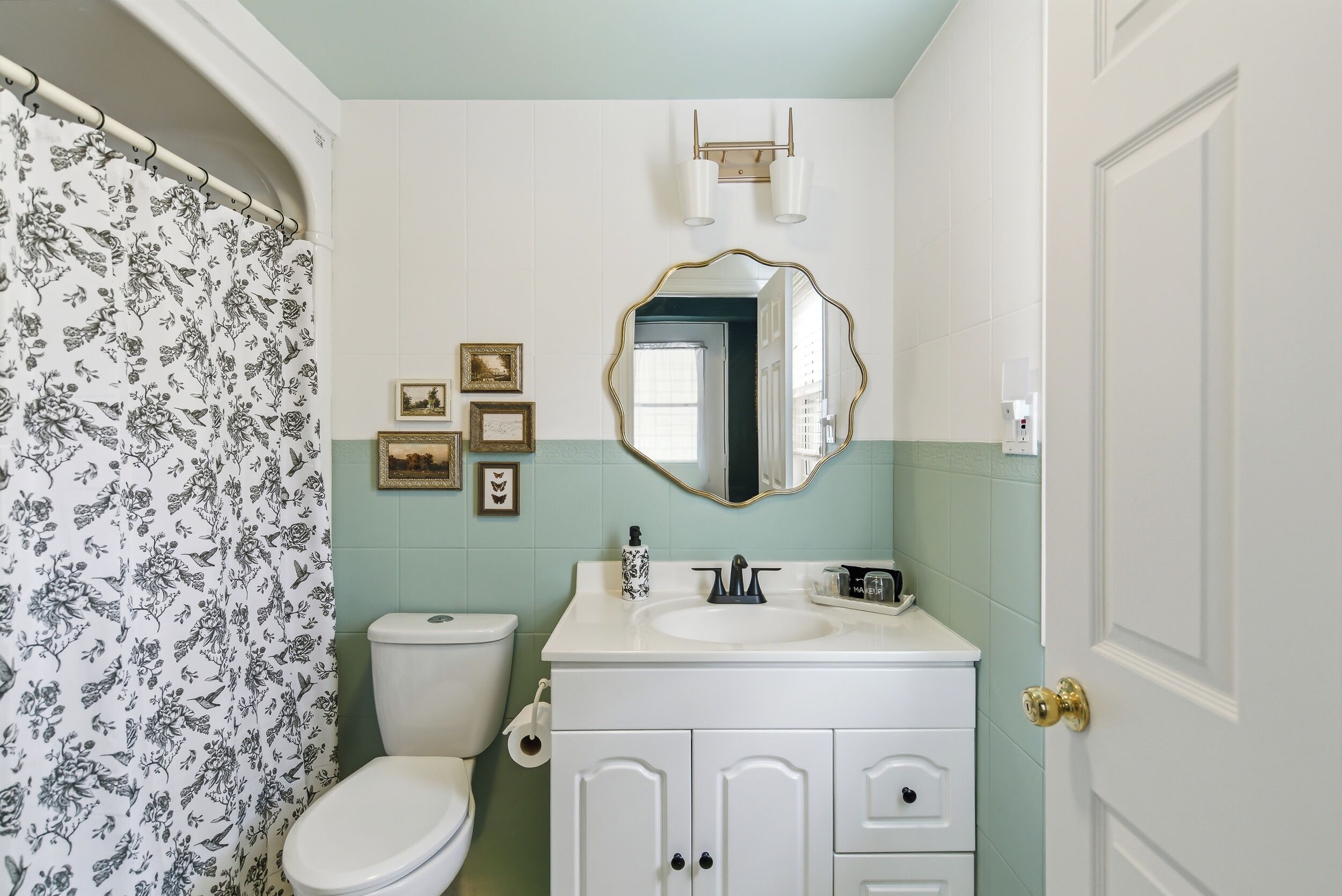 A bathroom with a toilet, sink, mirror, and framed pictures on the wall.