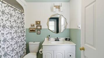 A bathroom with a toilet, sink, mirror, and framed pictures on the wall.
