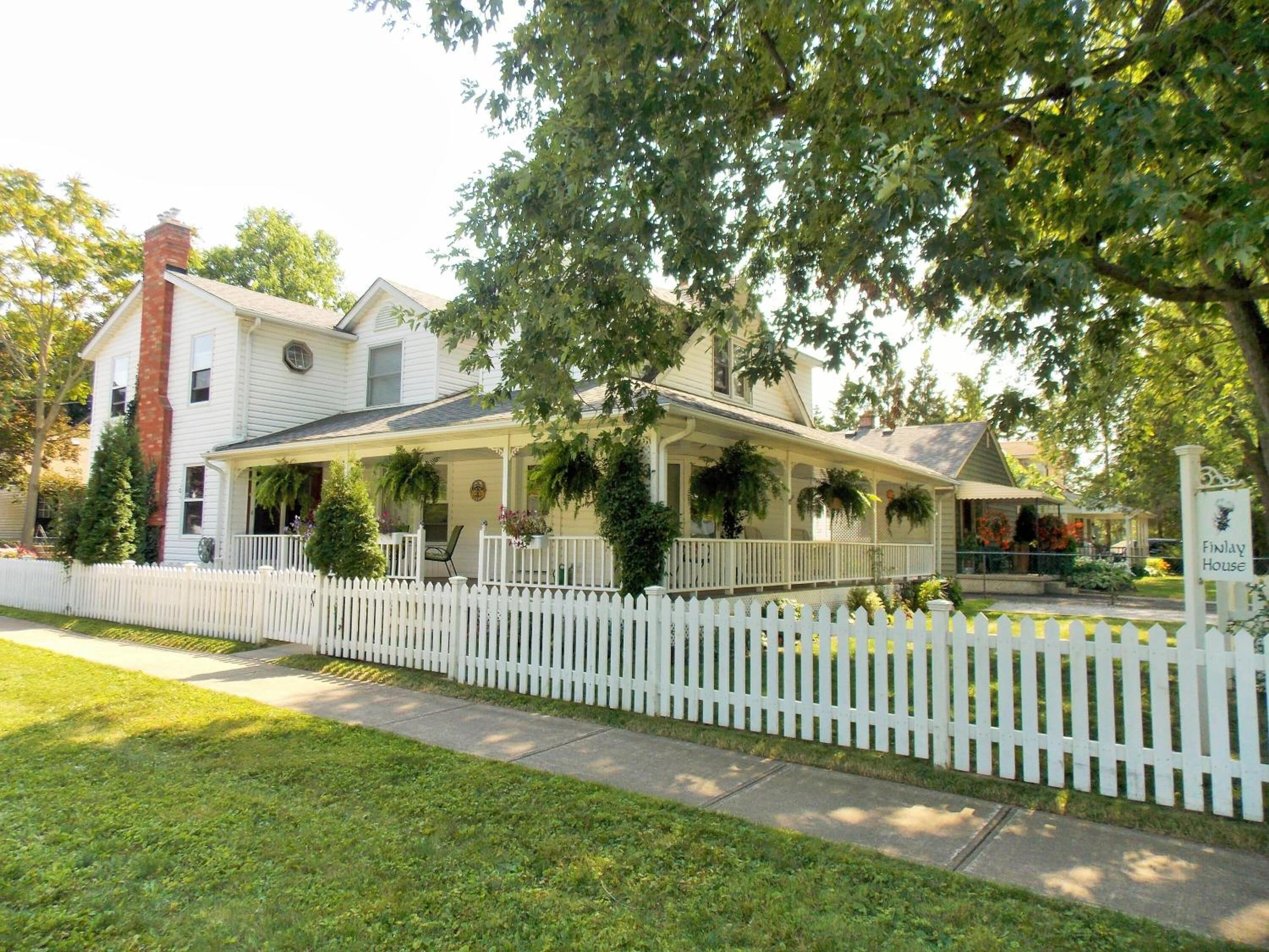 A two-story house with a porch, a white picket fence, and a sign that reads "Finlay House."