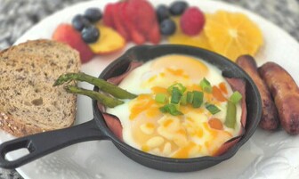 Una sartén con huevos y verduras, acompañada de tostadas y fruta en un plato.