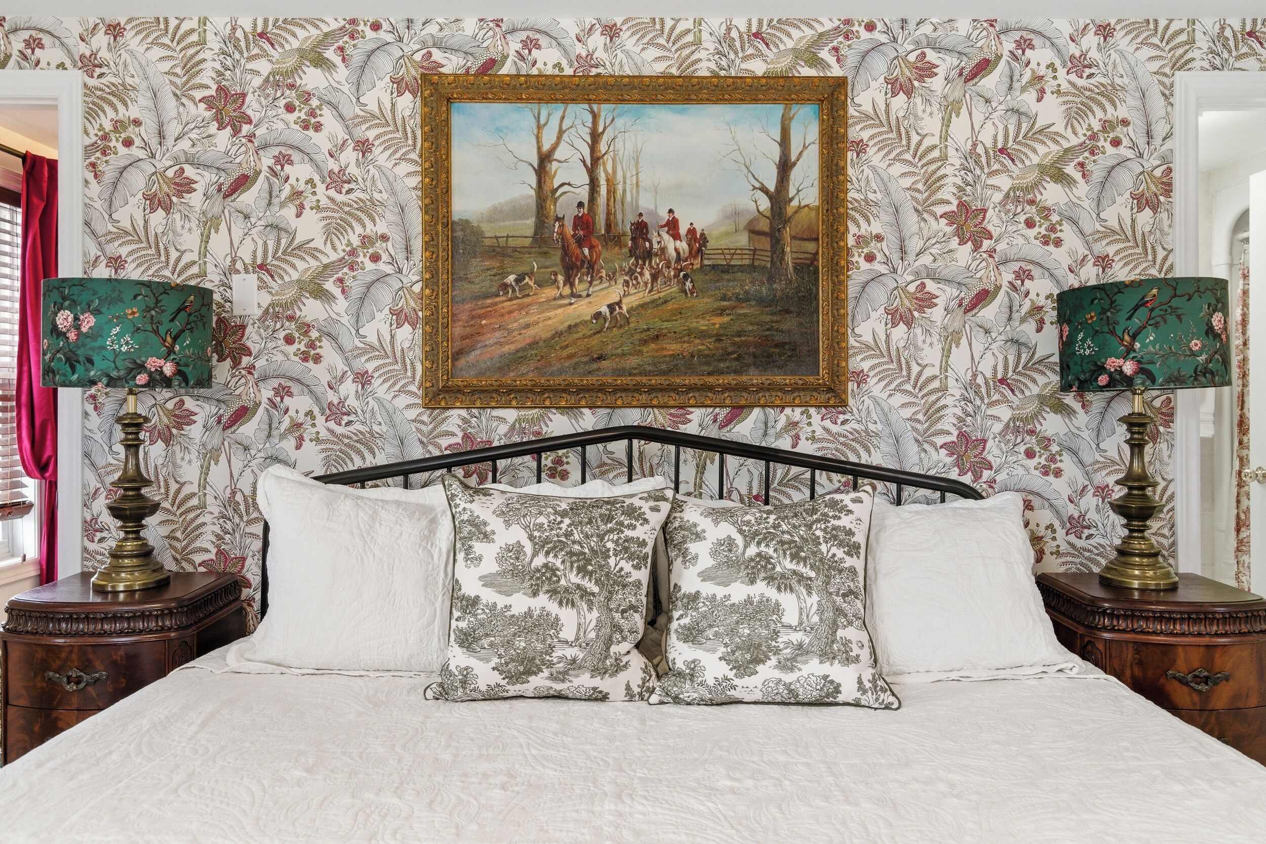 Un dormitorio con una cama, dos mesitas de noche, un cuadro y papel tapiz con motivos florales.