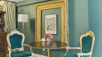 A dining area with a round table, two chairs, a framed artwork, and a lamp.
