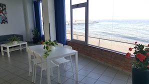 Une pièce avec une table et des chaises blanches, un petit canapé blanc et une grande fenêtre donnant sur la mer.