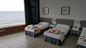Une chambre d’hôtel avec deux lits, une fenêtre donnant sur la mer et deux tableaux encadrés accrochés au mur.