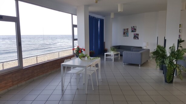 Un salon avec vue sur la mer, un coin repas avec des meubles blancs et un canapé gris.