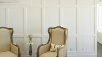 A room with two armchairs, a small table with a vase, and a white paneled wall.